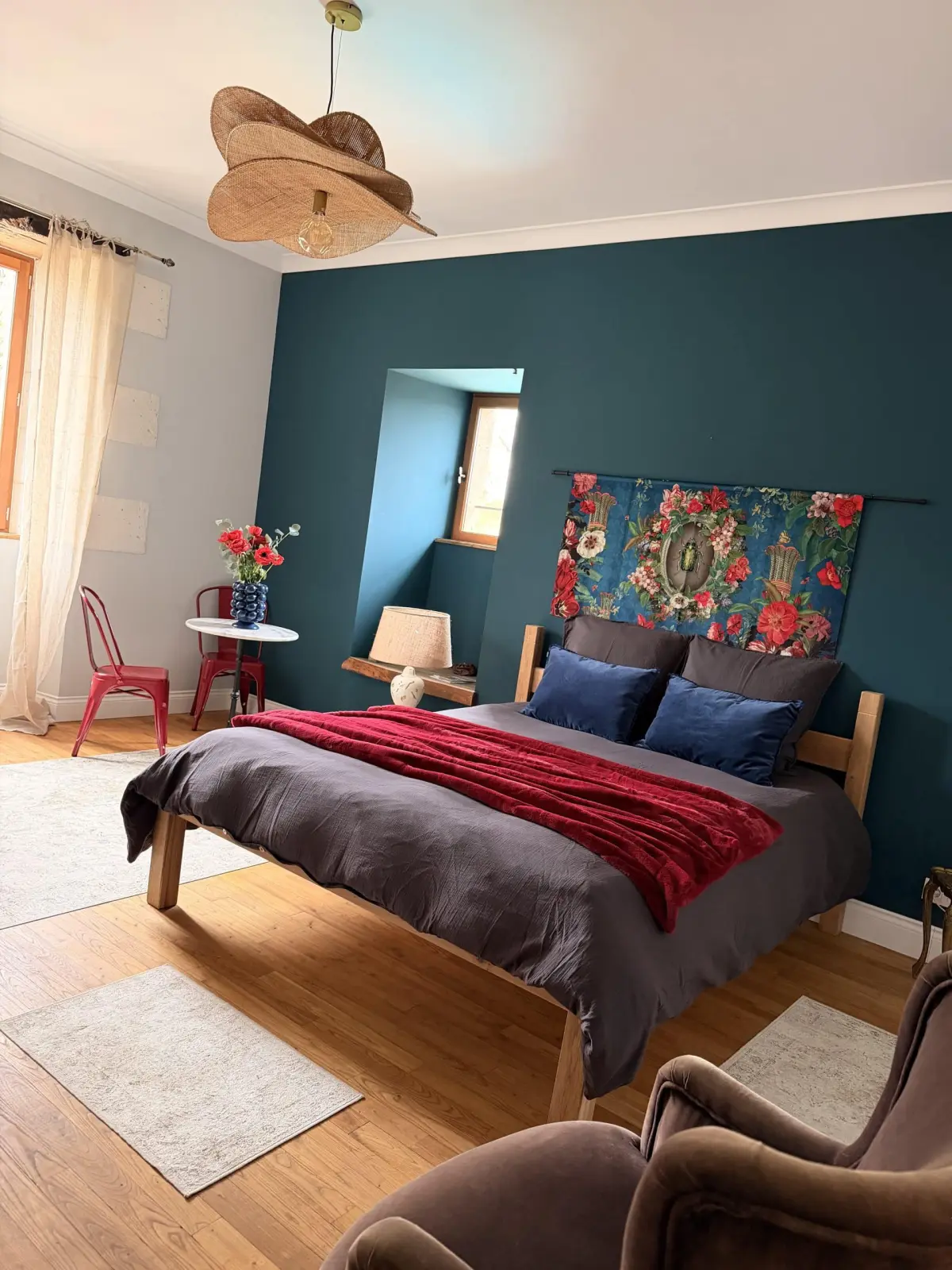 Bedroom at Le Patio Bleu with a double bed, red throw, floral hanging, blue wall, red chairs and armchair