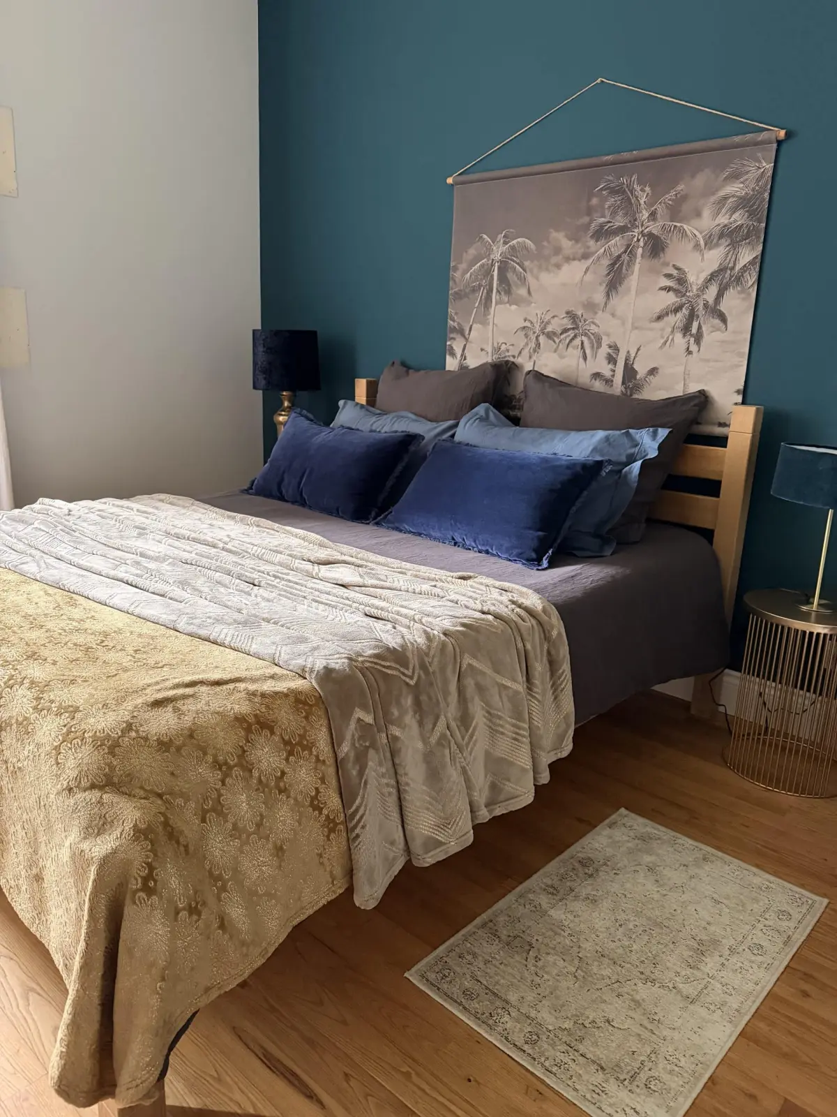 Bedroom at Le Patio Bleu with a double bed, blue cushions, palm-print hanging and a teal wall