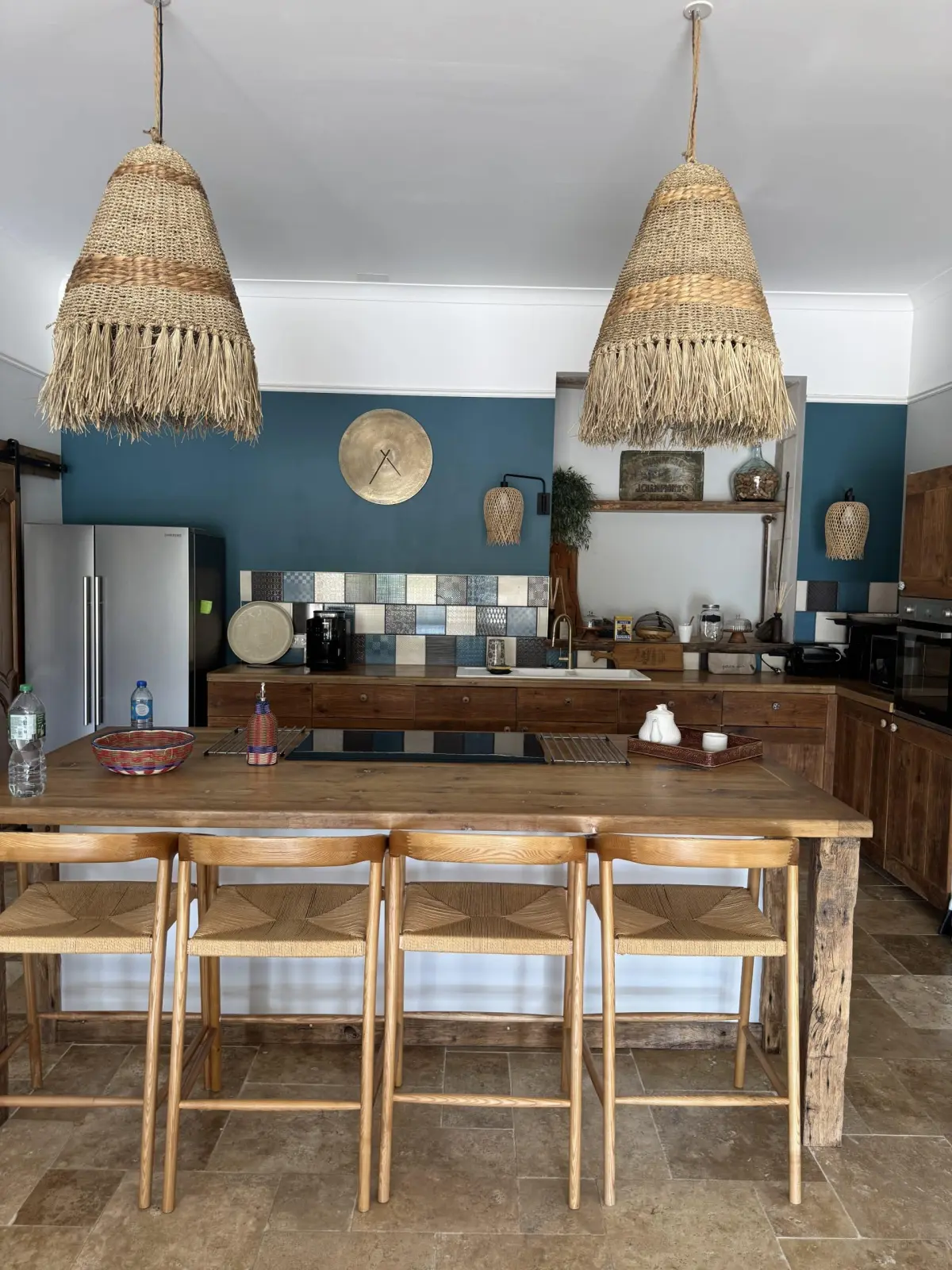 Kitchen at Le Patio Bleu with a wooden island, rush-seat stools, raffia pendant lamps and a blue wall