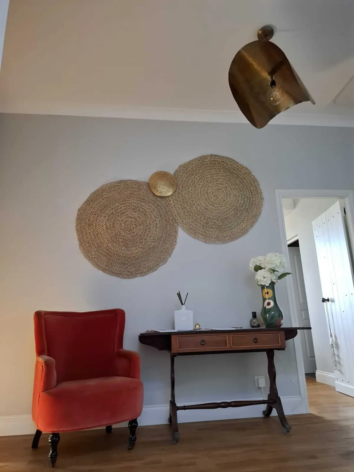 Red armchair and wooden console beneath woven straw wall decorations at Le Patio Bleu