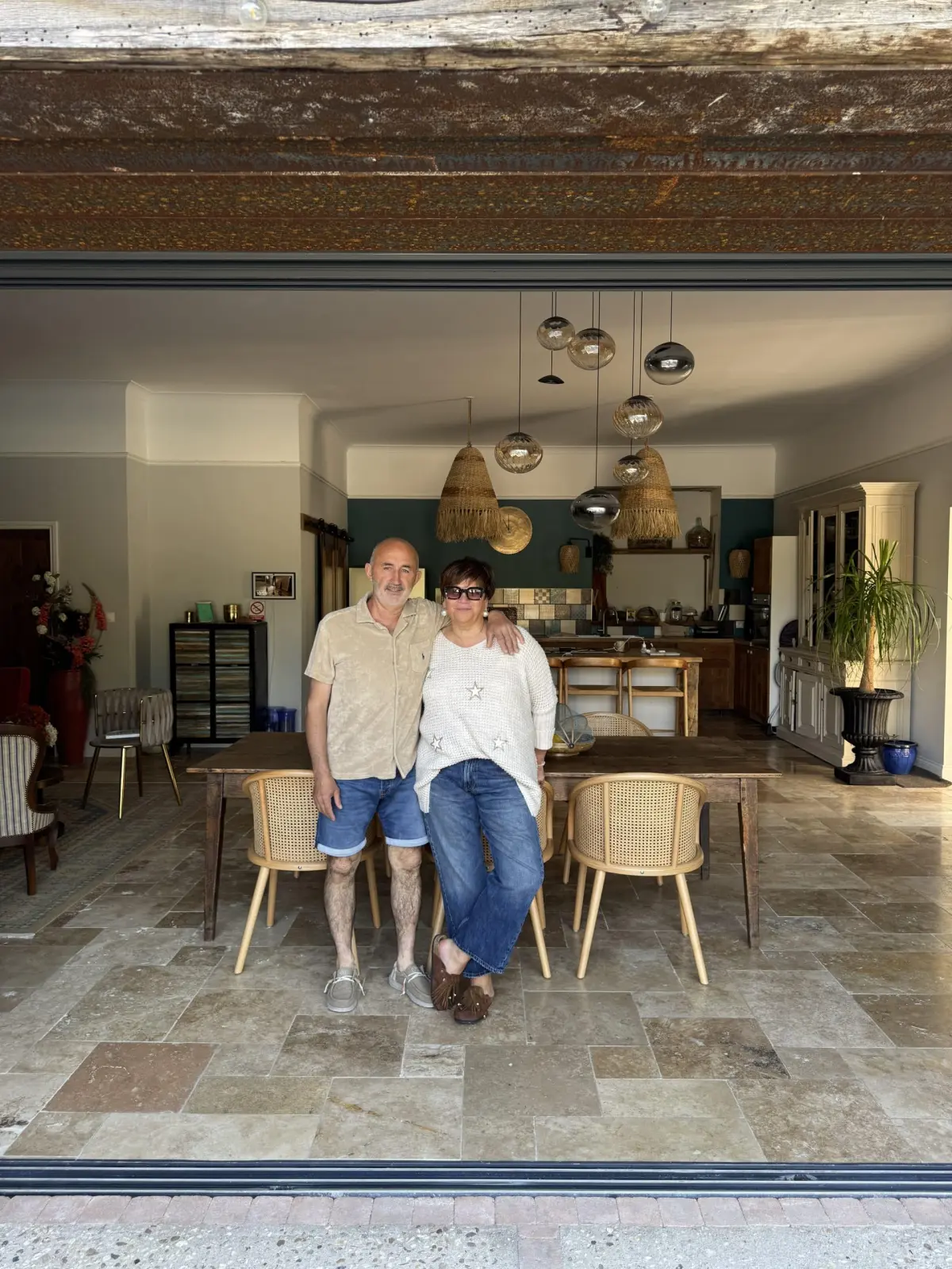 The two hosts of Le Patio Bleu standing in the living area in front of the table and kitchen