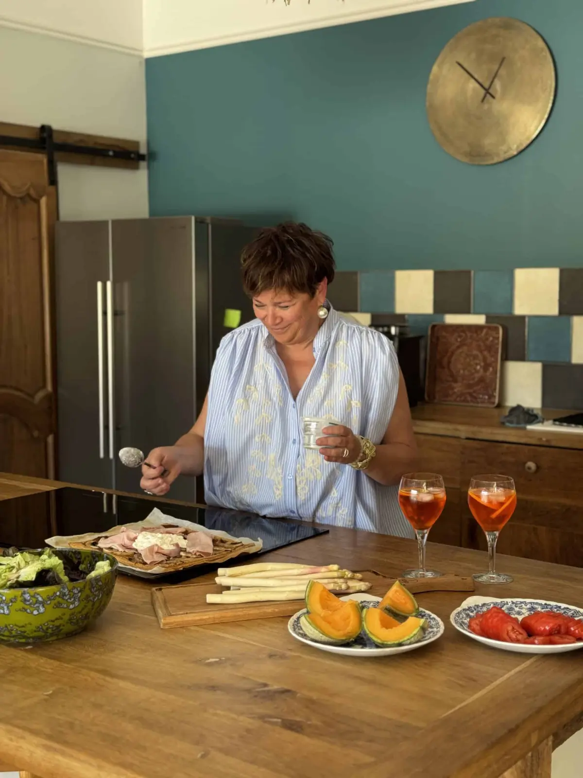 Hostess at Le Patio Bleu preparing a platter of cured meats beside melon and two spritzes in the kitchen