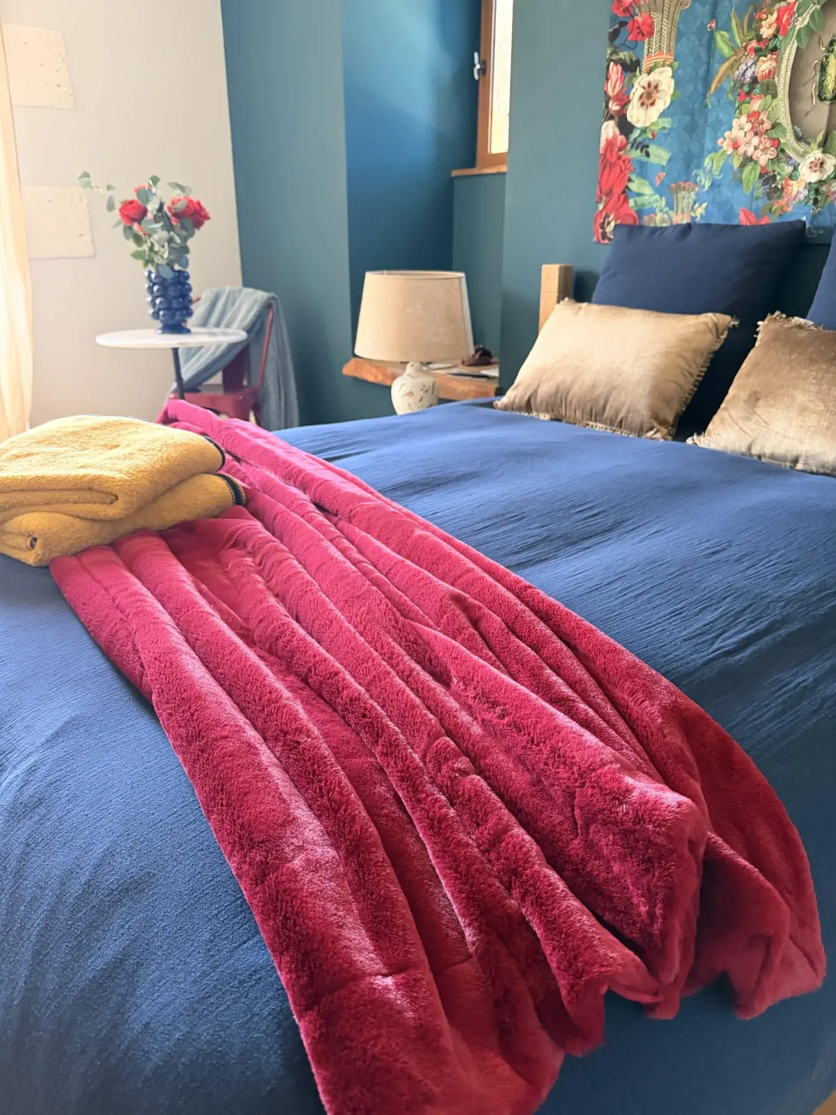 Bed at Le Patio Bleu with a blue duvet, raspberry pink throw, yellow towels and a floral hanging