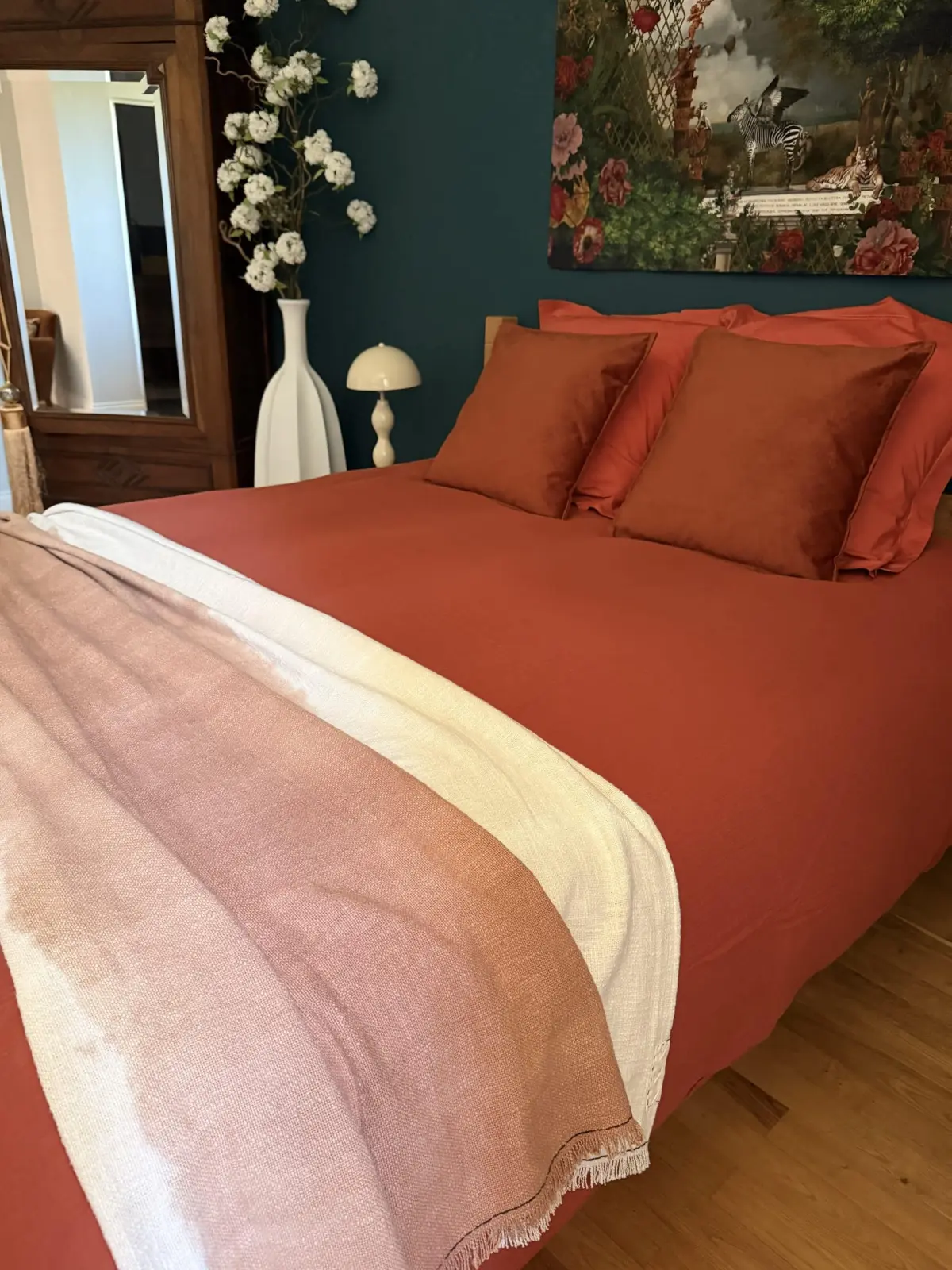 Bed at Le Patio Bleu with rust-coloured linen and a pink and white throw against a dark blue wall and hanging