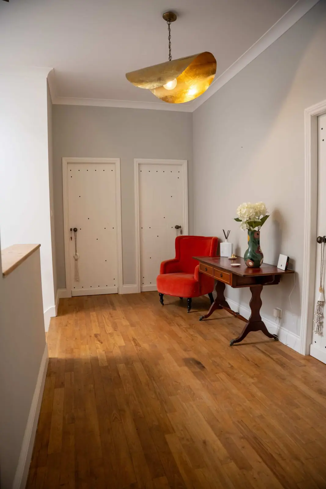 Landing at Le Patio Bleu with wooden floor, red armchair, wooden console, bouquet and gold pendant light