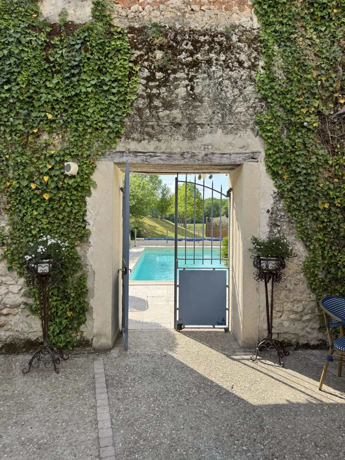 Open doorway in an ivy-covered stone wall looking through to the pool at Le Patio Bleu