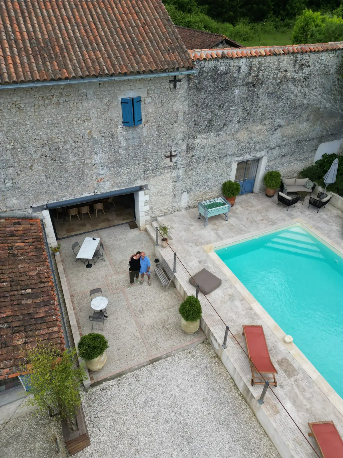 Aerial view of Le Patio Bleu: stone house with blue shutters, courtyard, pool, sun loungers and two hosts