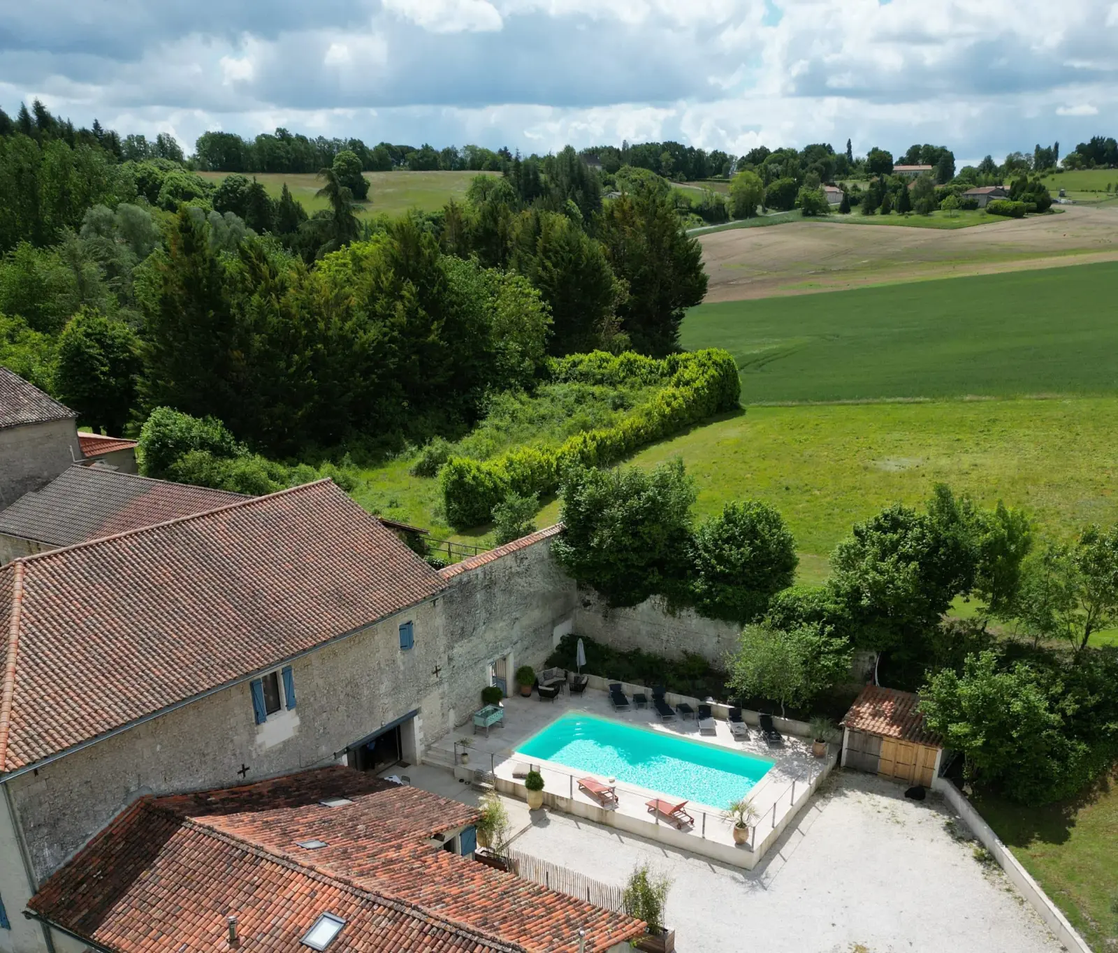 Aerial view of Le Patio Bleu: stone house, courtyard pool, garden, hedges and rolling fields