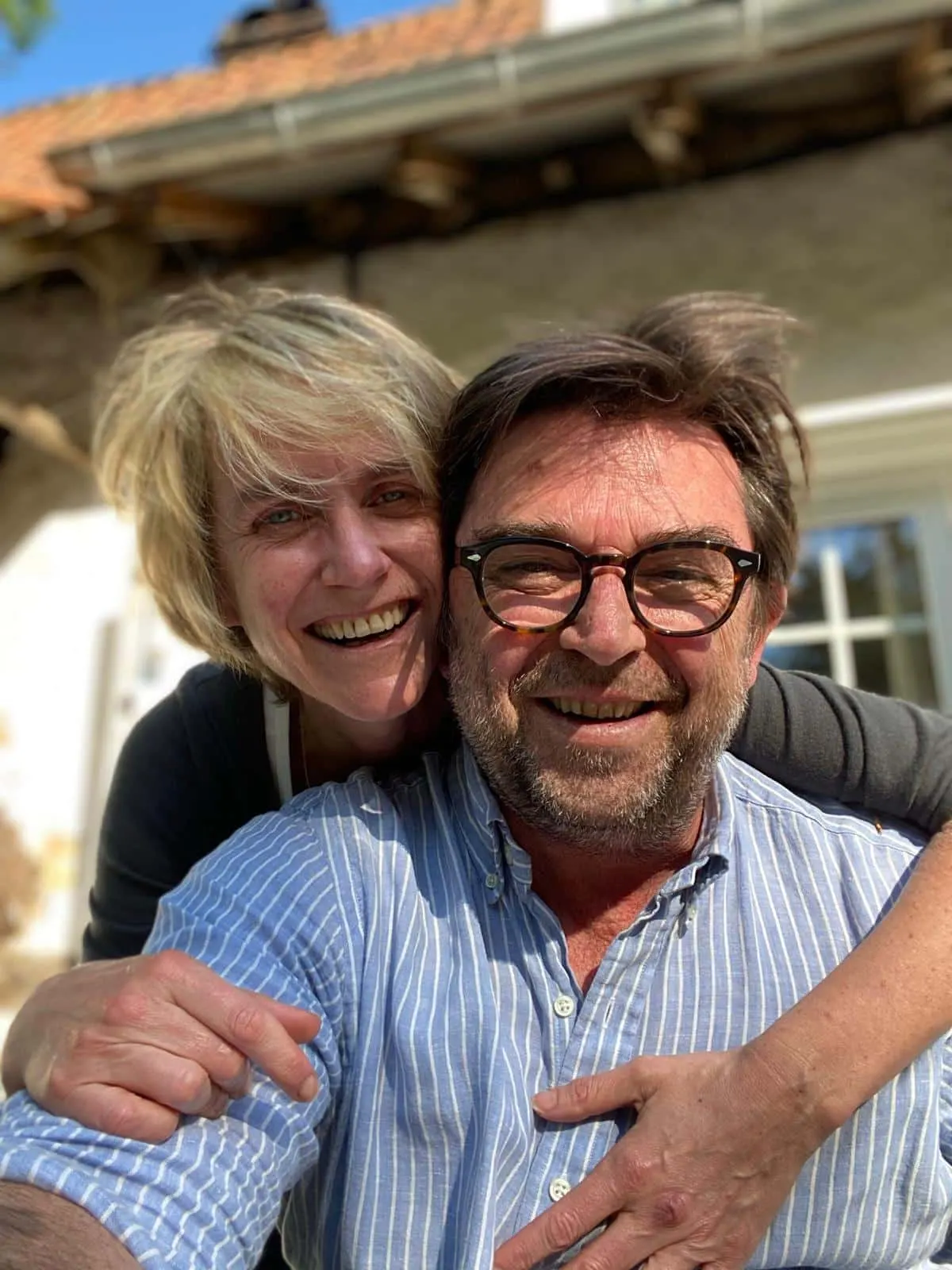 Smiling couple embracing in the sunshine in front of a tiled-roof house, La Plonplonière