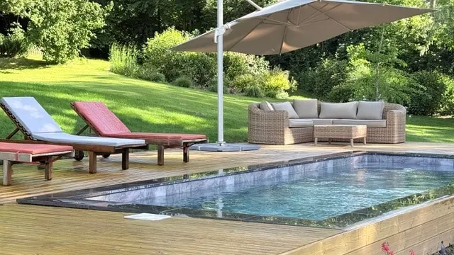 Pool on timber decking, sun loungers, a cantilever parasol and woven resin garden furniture, La Plonplonière
