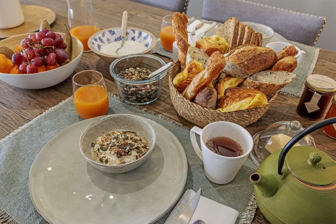 Breakfast table at La Plonplonière: bread basket, fruit, muesli, orange juice and a green teapot