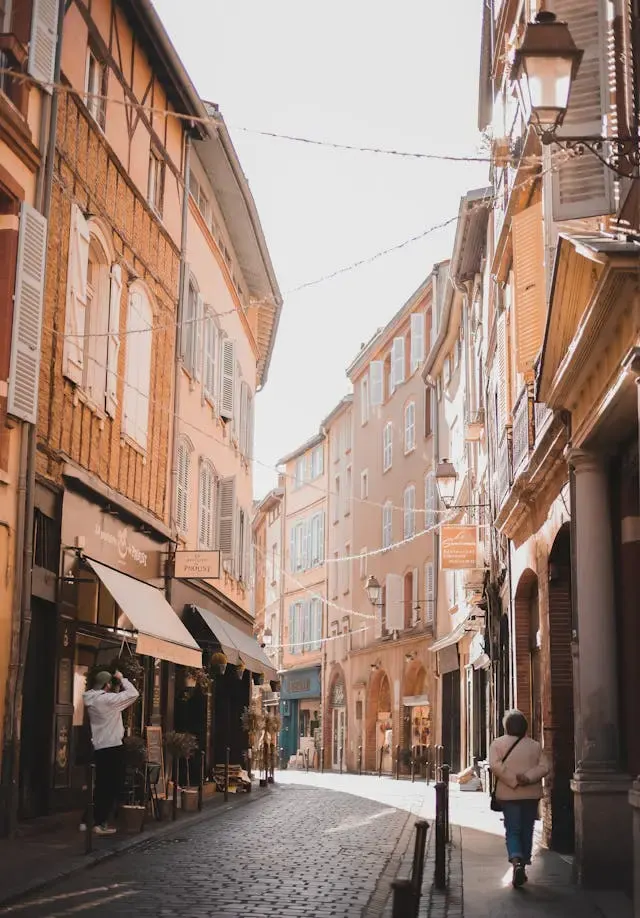 Rue pavée bordée de façades en brique et pans de bois, lampadaires et passants