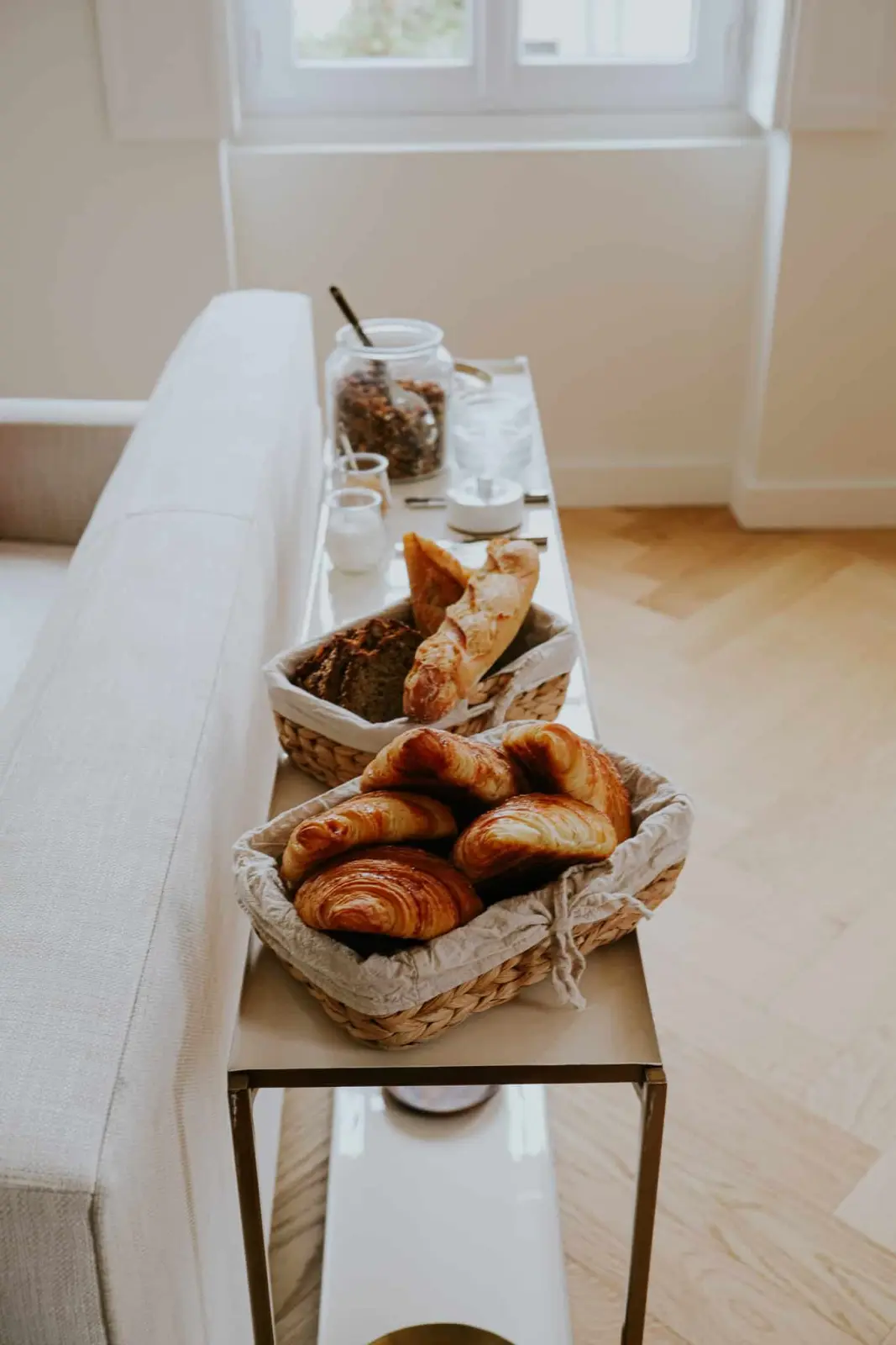 Baskets of croissants and bread on a console table beside a sofa, Les Séraphines