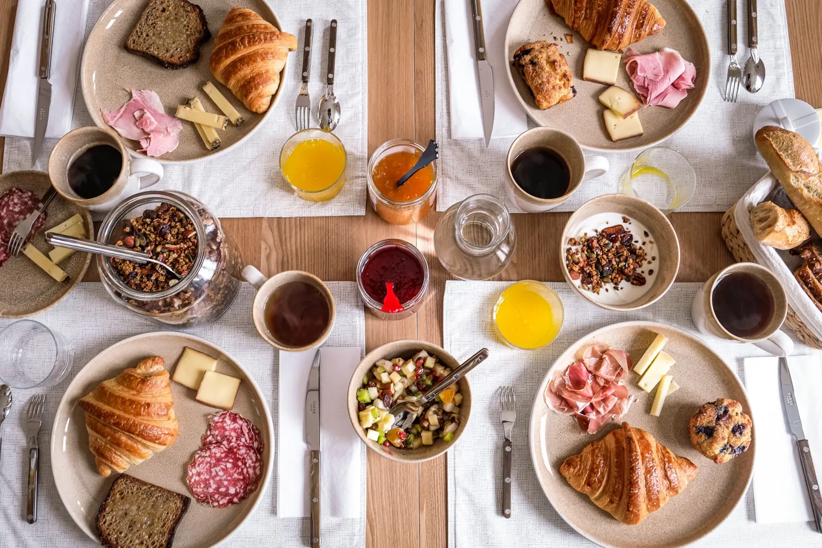 Petit-déjeuner des Séraphines vu du dessus : croissants, charcuterie, fromage, granola et café