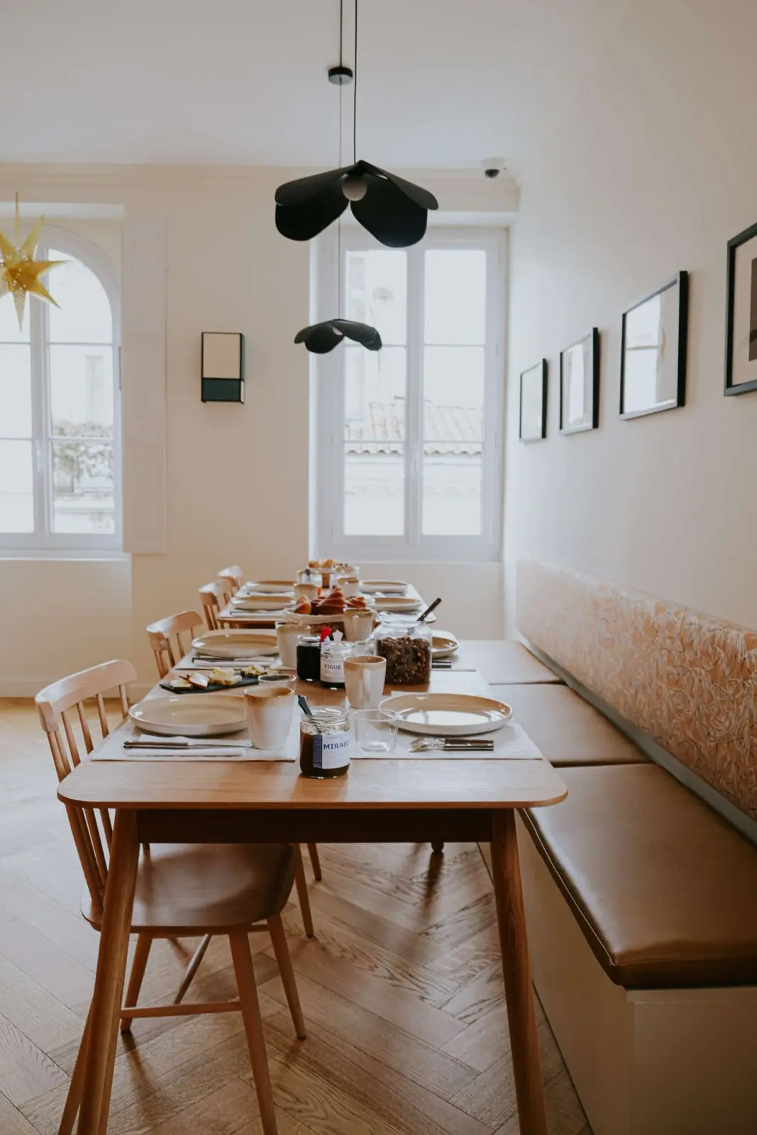 Breakfast room with a long laid table, wooden chairs, bench seating and tall windows, Les Séraphines