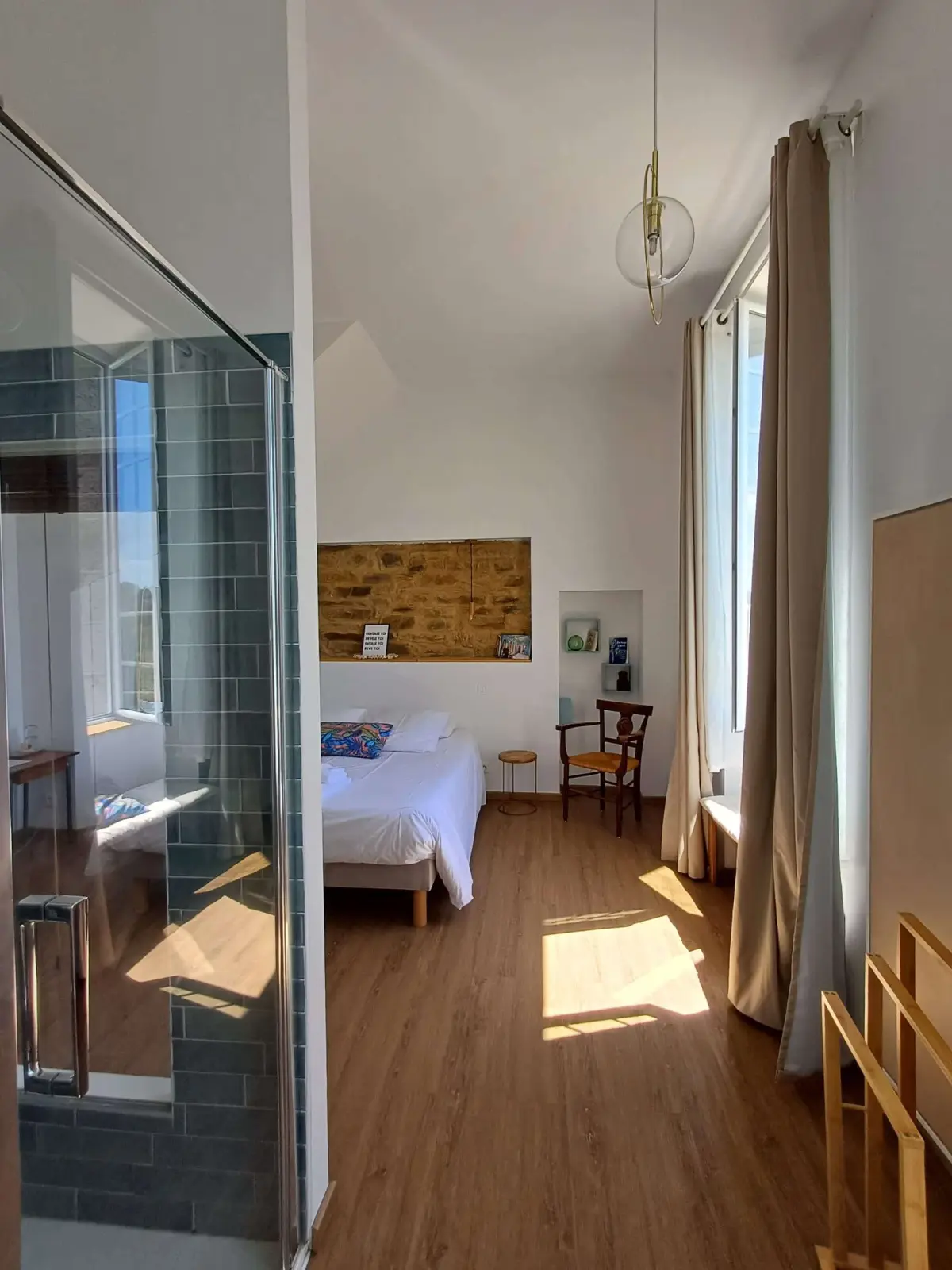 Bouli Boula room at Ty Monde: double bed below a stone niche, glass shower and sunlit wooden floor
