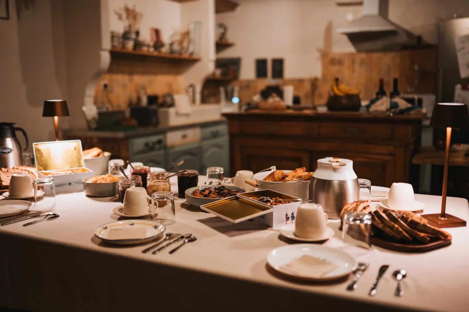 Breakfast buffet laid on a cloth-covered table in front of the kitchen, lamps lit, Ty Monde