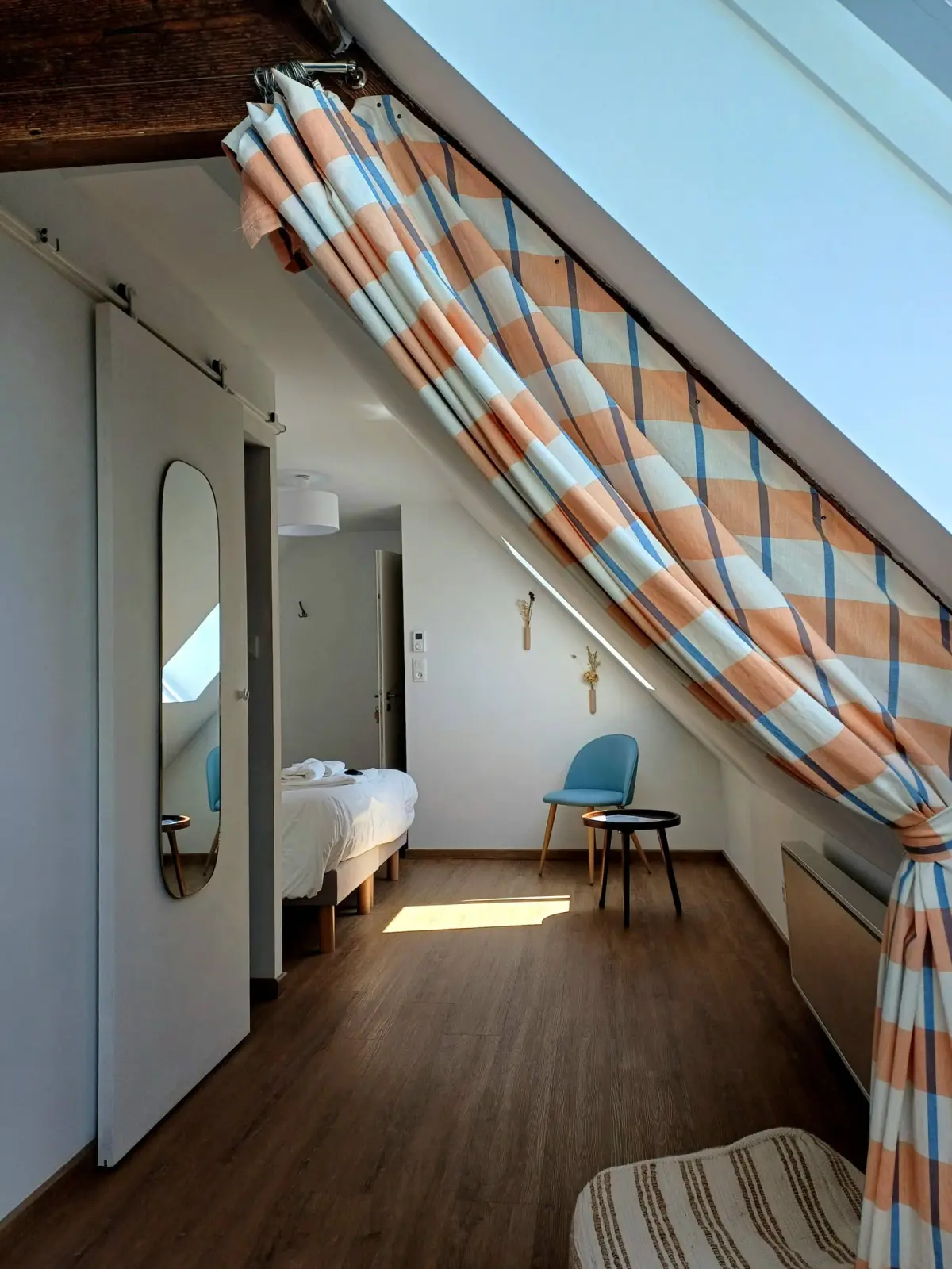 Cocotte attic room at Ty Monde with an orange and blue checked curtain, wooden floor and blue chair