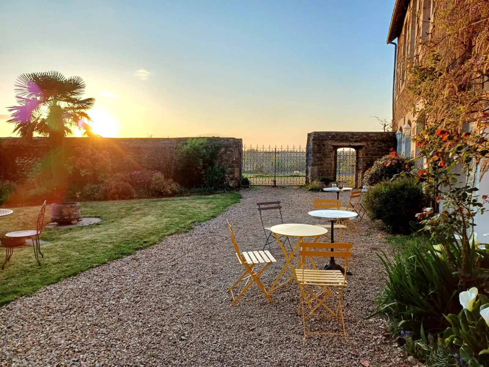 Gravel courtyard with yellow tables and chairs, palm tree and stone wall at sunset, Ty Monde