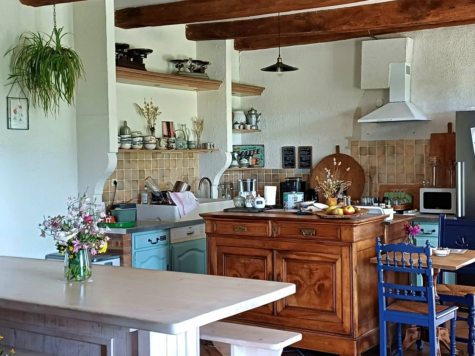 Kitchen-diner at Ty Monde with beams, wooden dresser, laden shelves and blue chairs