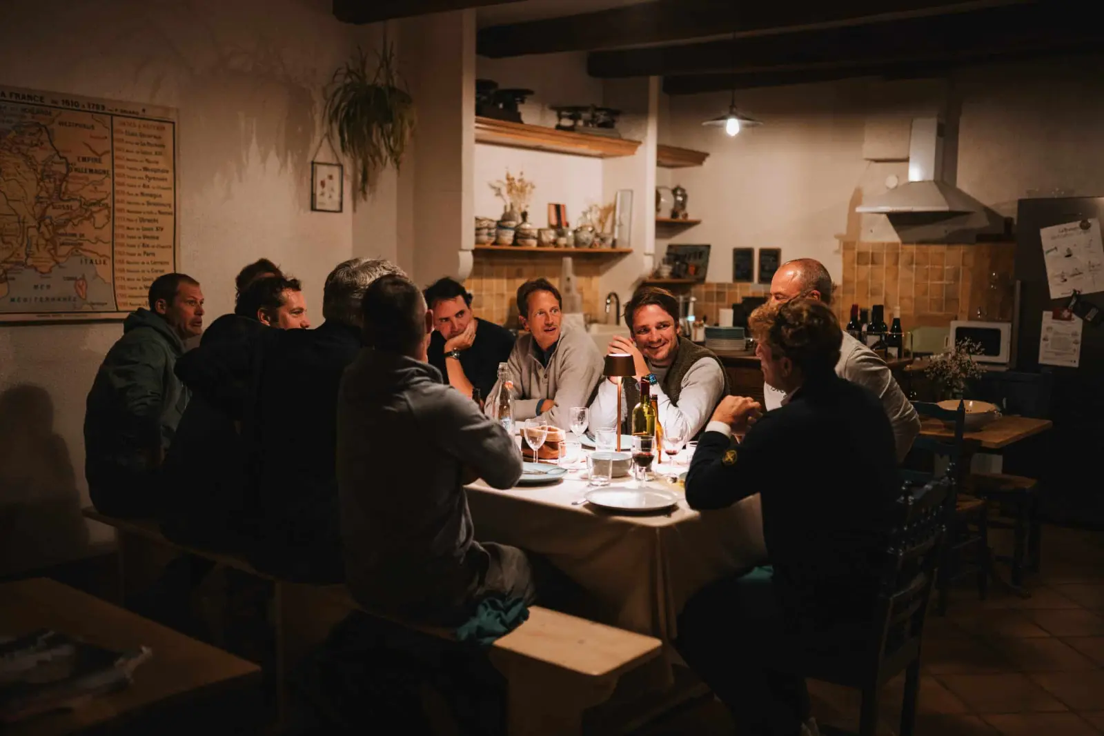Table of men sharing an evening meal in the kitchen with laden shelves, Ty Monde
