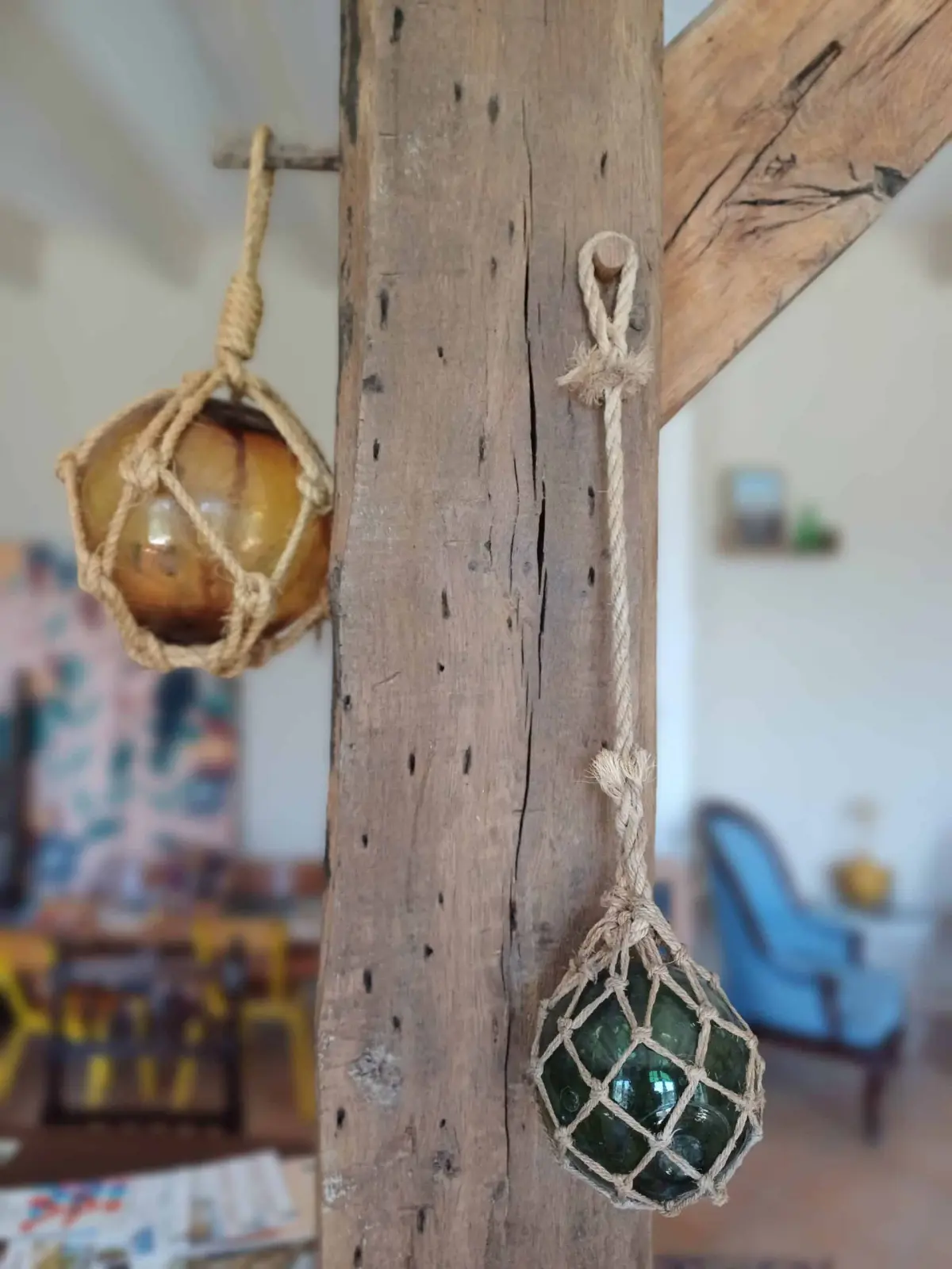 Amber and green glass fishing floats in rope nets hanging from a wooden beam, Ty Monde