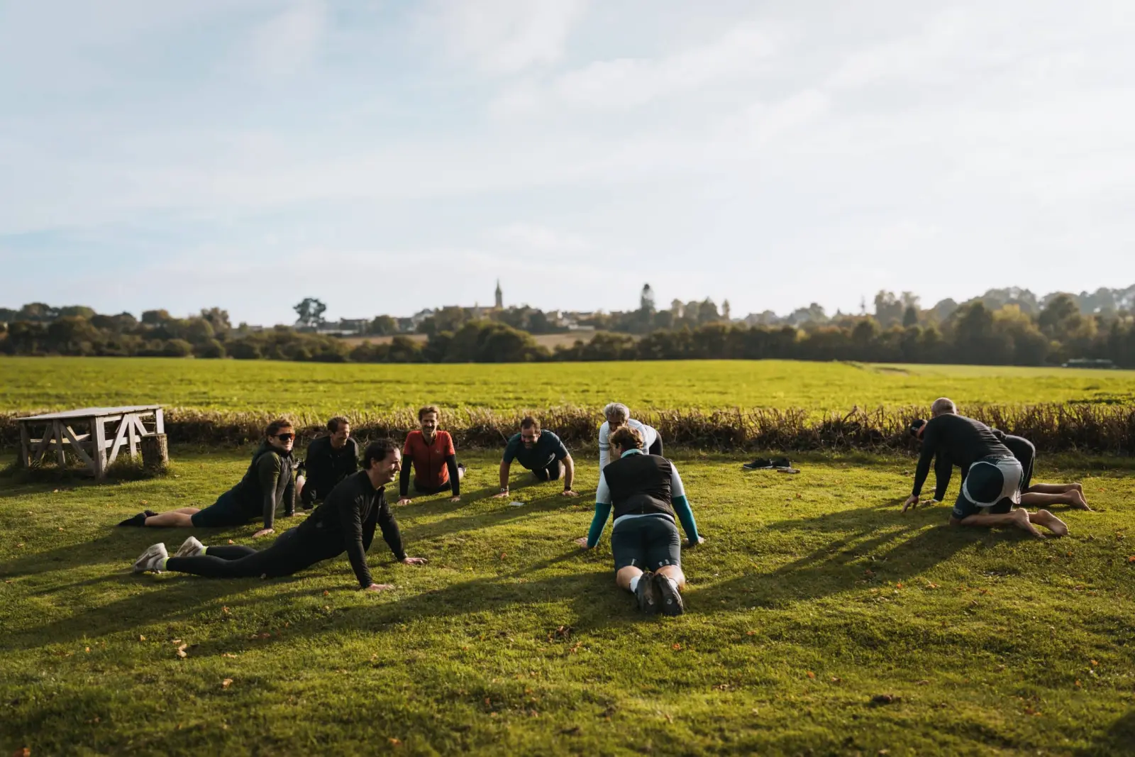 Group doing stretches on the grass in the sunshine in front of a field, at Ty Monde