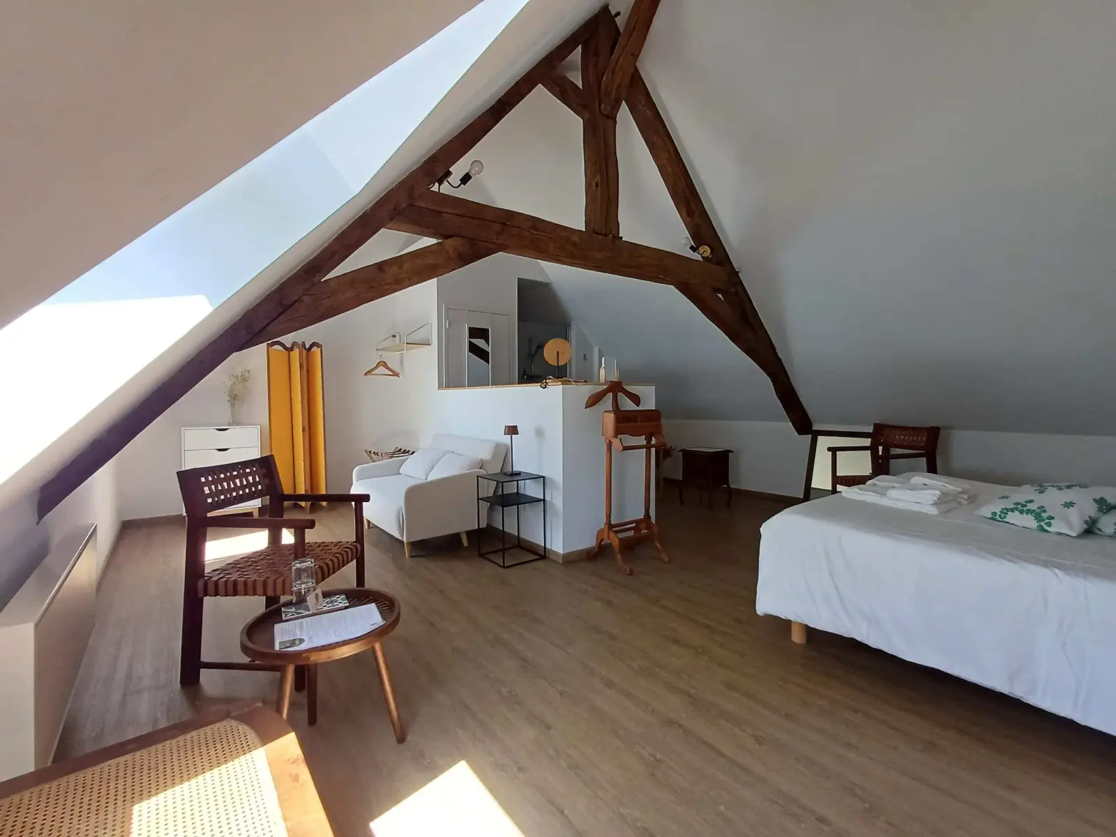 Insoupçonnée room at Ty Monde under exposed beams: double bed, wooden armchair and white sofa