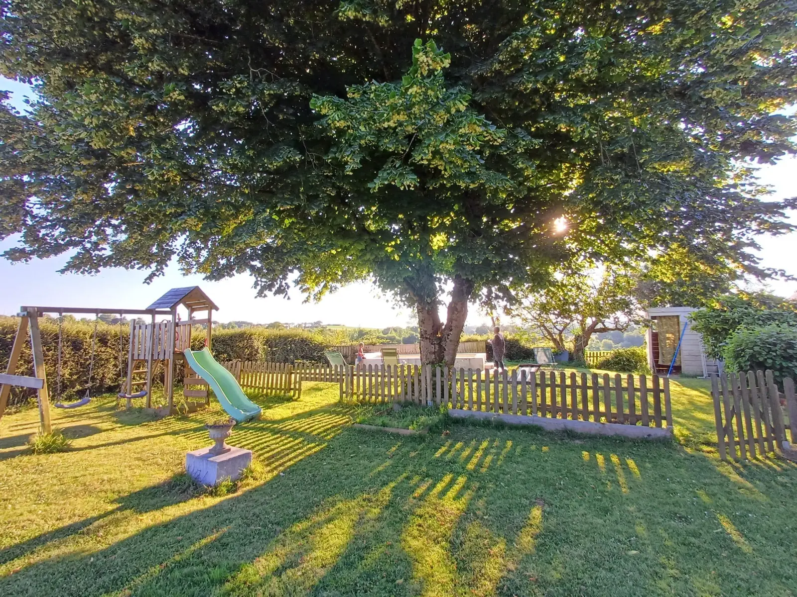Ty Monde garden shaded by a large tree, play area with slide and swing, wooden fence