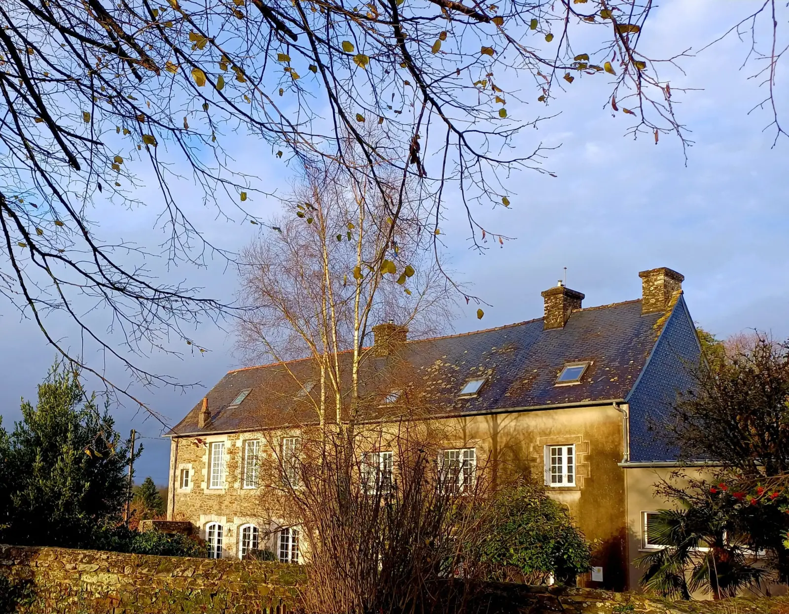 Large stone house with slate roofs and chimneys in autumn sunshine, Ty Monde