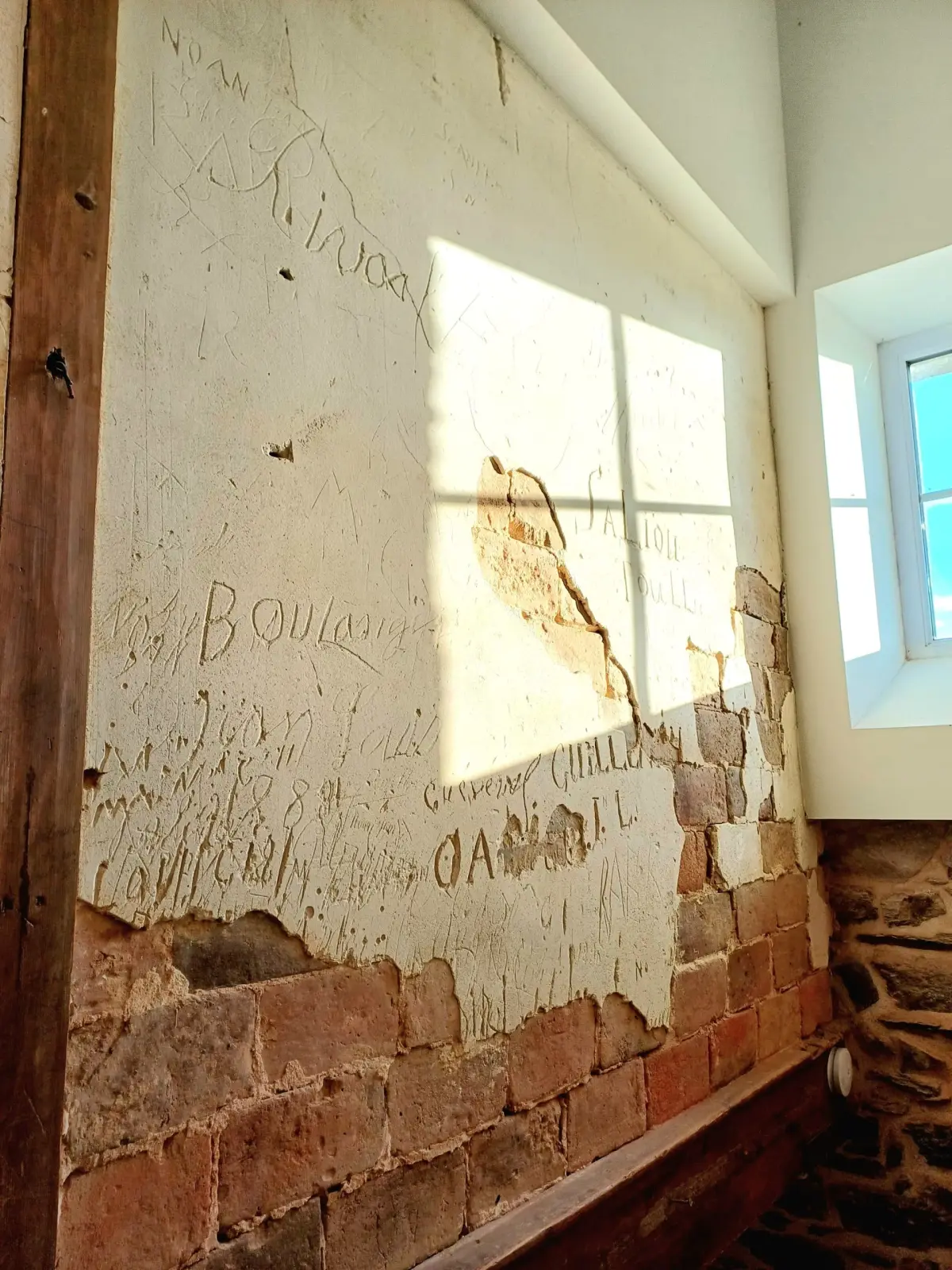 Old wall with flaking plaster covered in hand-carved names, exposed brick below, Ty Monde