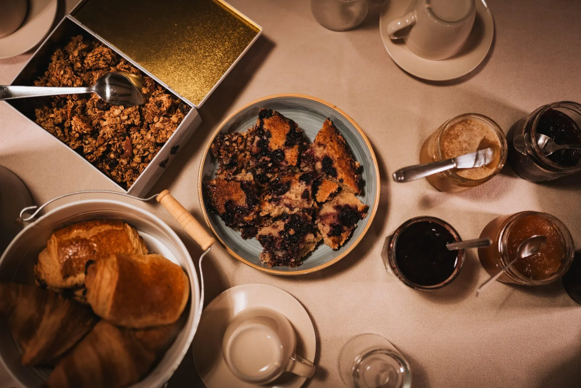 Petit-déjeuner vu du dessus à Ty Monde : granola, gâteau aux myrtilles, croissants, confitures et tasses