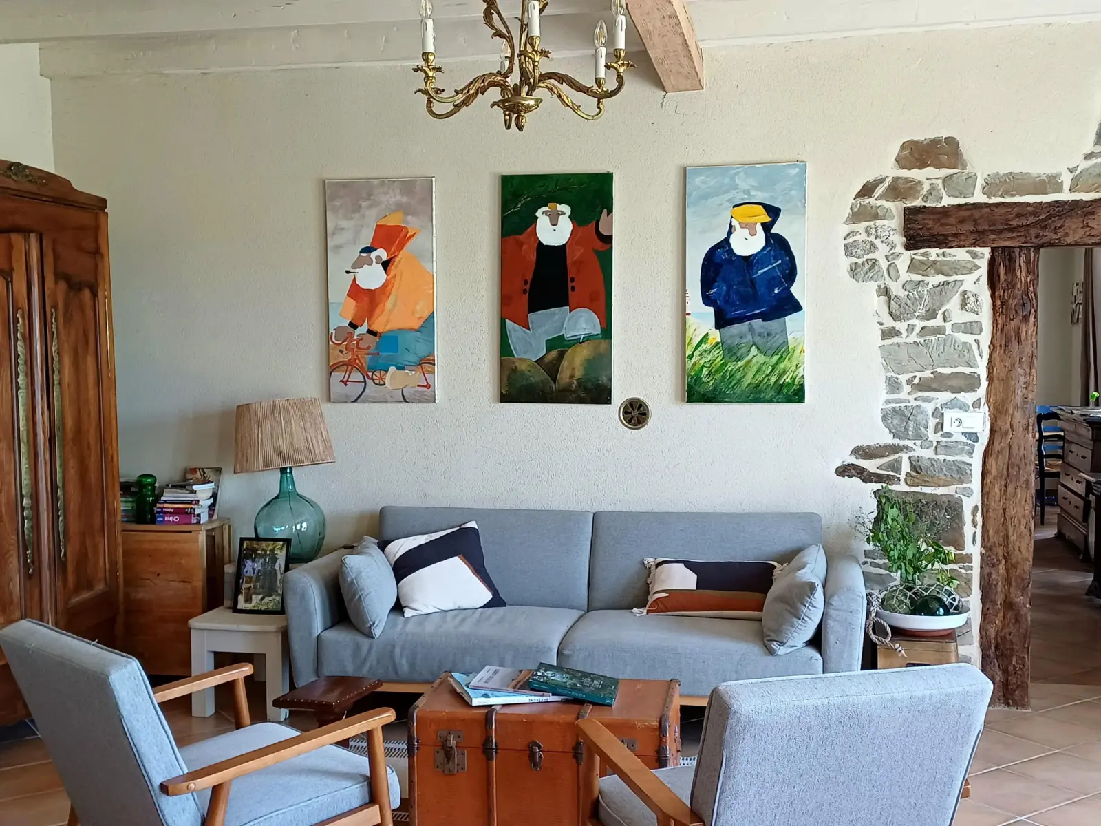 Sitting room at Ty Monde with grey sofa, wooden trunk, three paintings of sailors and stone wall