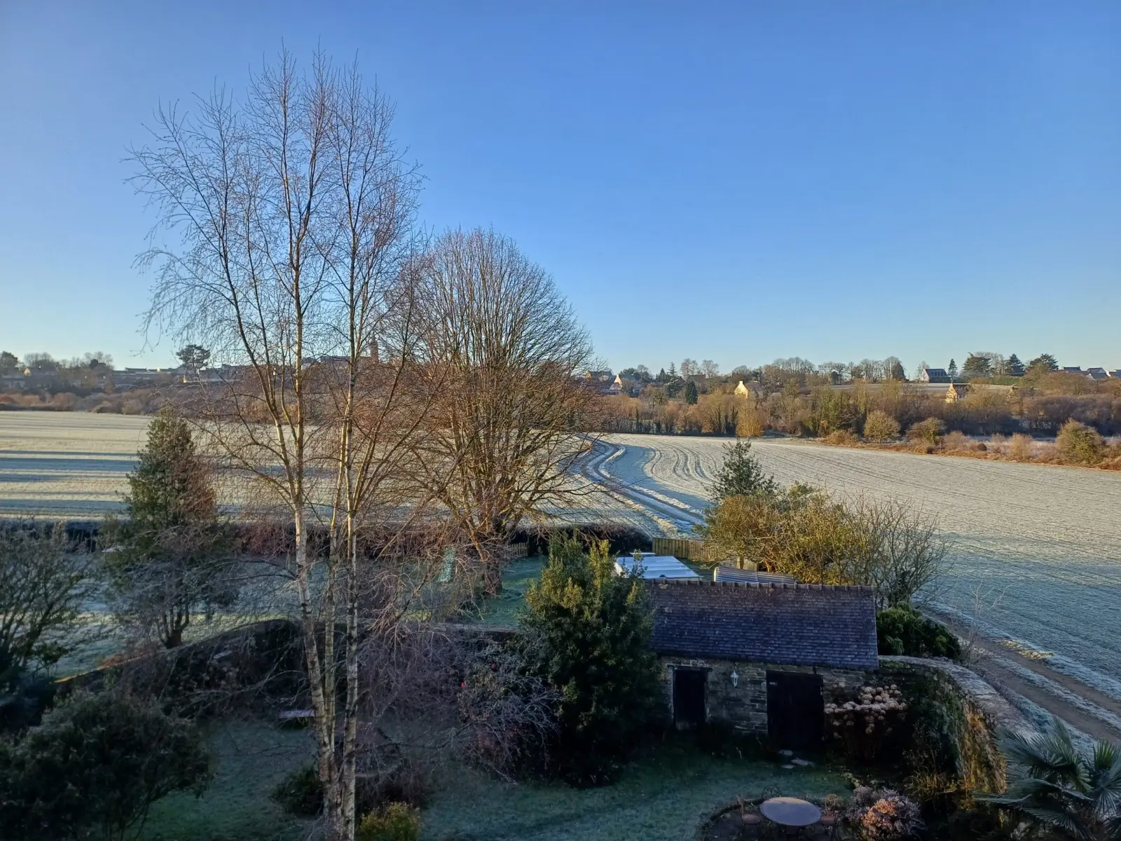 View over the garden, a stone outbuilding and frosty fields under a blue sky, Ty Monde