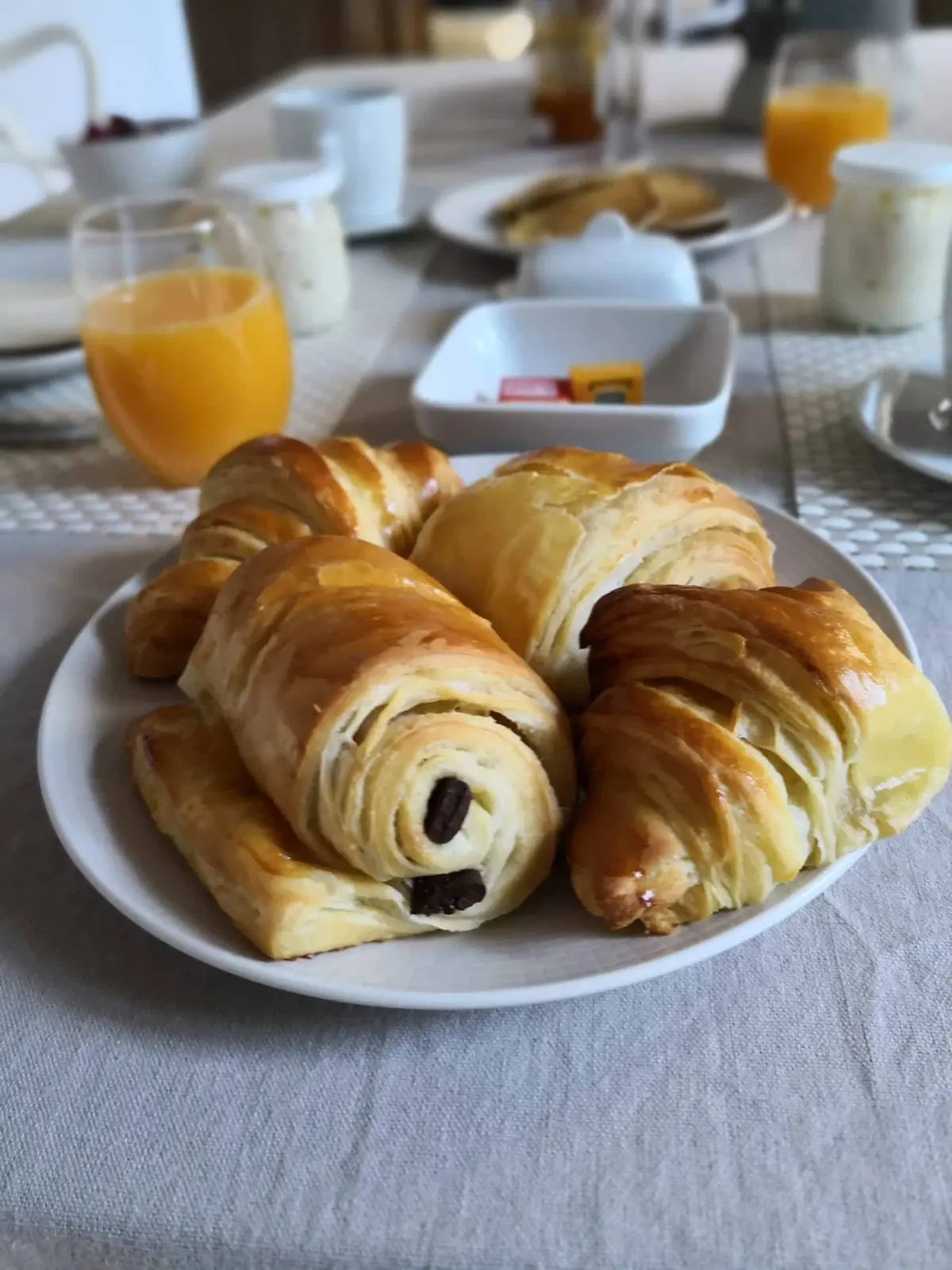 Plate of golden croissants and pains au chocolat, orange juice and jars on the breakfast table, La Vie Voyage