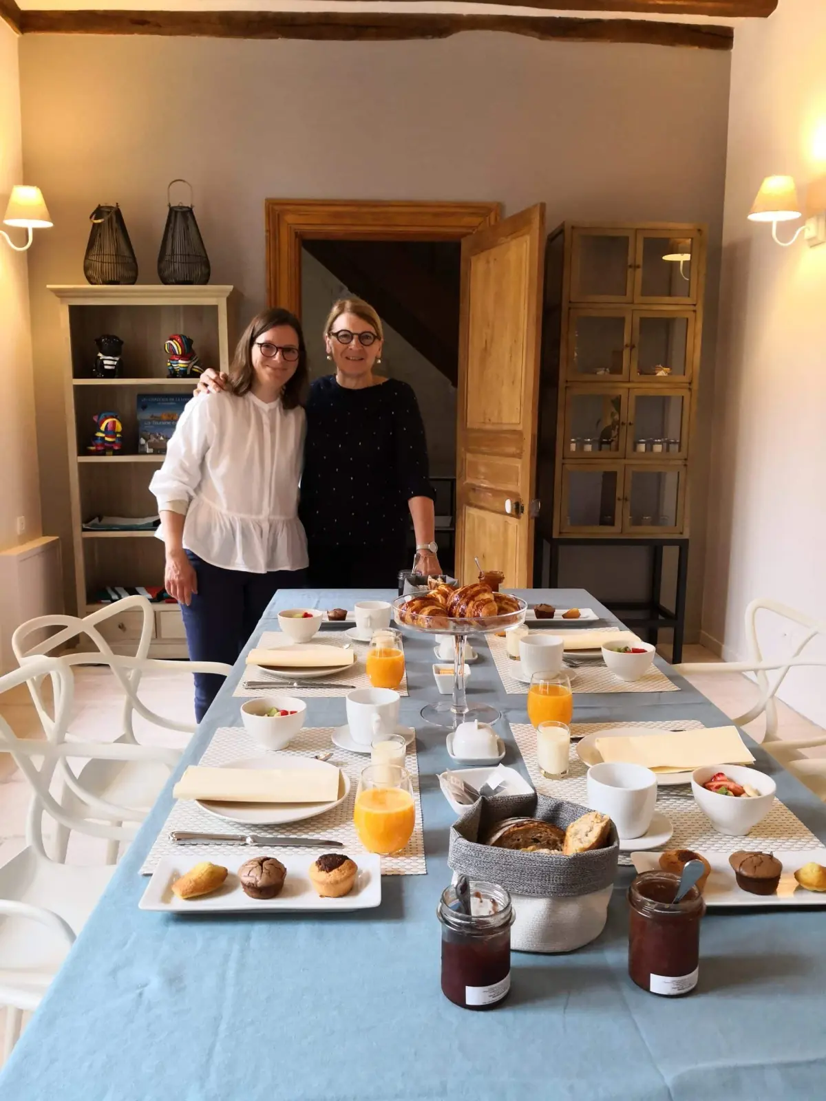 Two hostesses standing at the end of a long breakfast table laid beneath the beams, La Vie Voyage