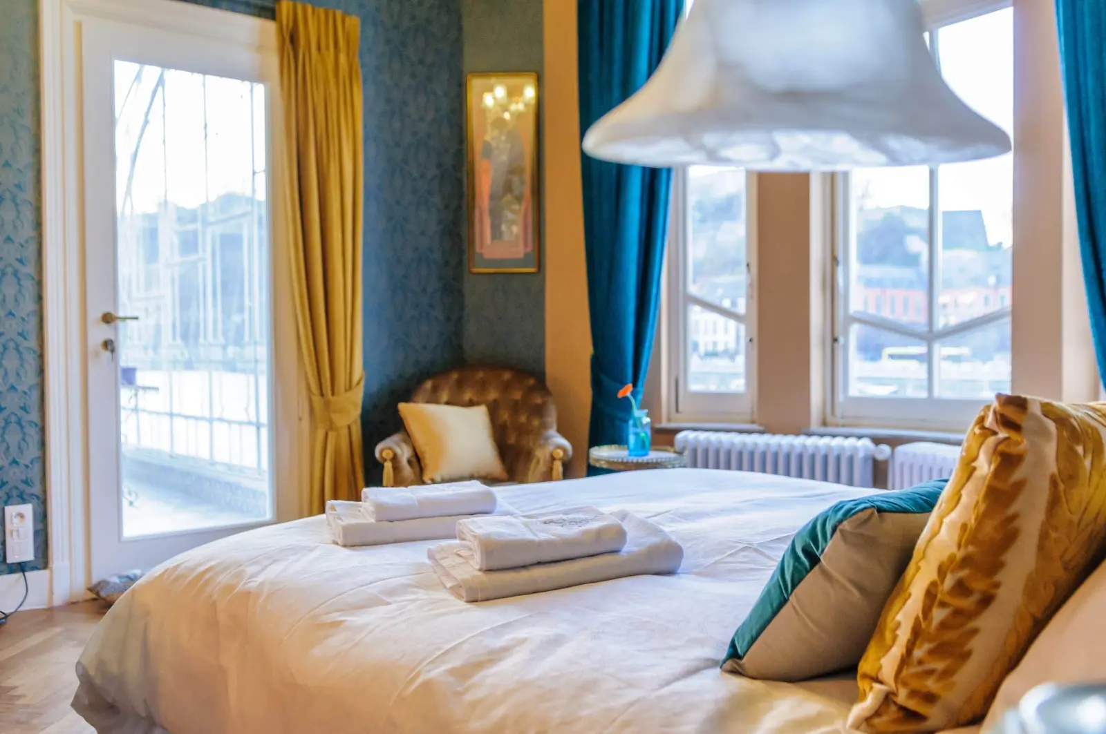 Bedroom at Villa Balat: bed with folded towels, blue wallpaper, yellow curtains and buttoned armchair