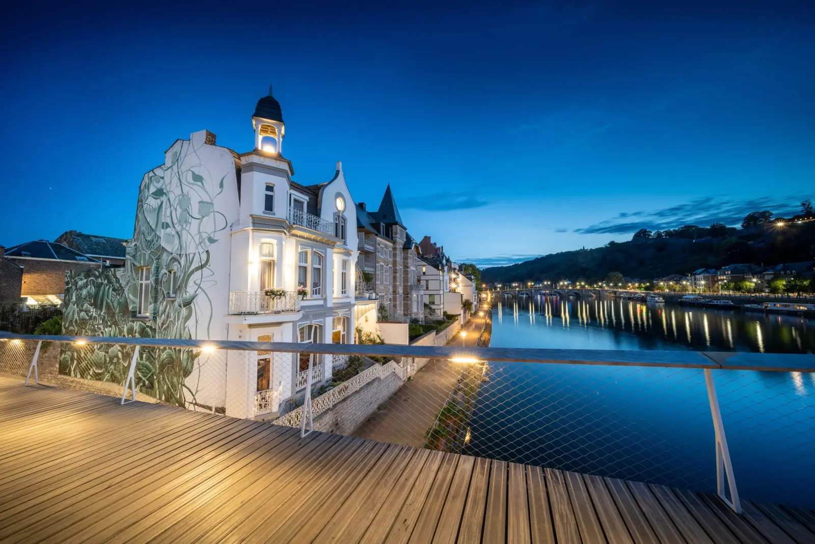 La Villa Balat illuminée la nuit, sa tourelle et sa fresque végétale, au bord de la rivière