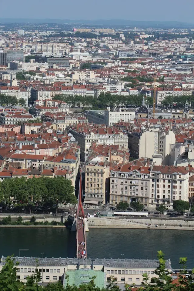 Vue plongeante sur une ville aux toits rouges, une passerelle rouge enjambant la rivière