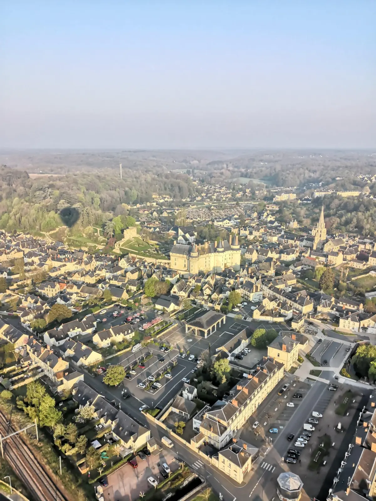 Vue aérienne d'une ville aux toits d'ardoise, avec son château, son clocher et la campagne boisée au loin